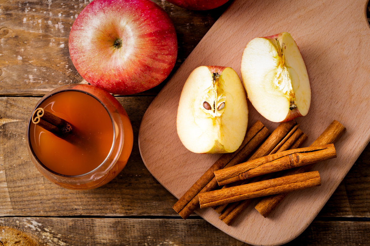 Apple cider with cinnamon sticks beside sliced apples on a board.