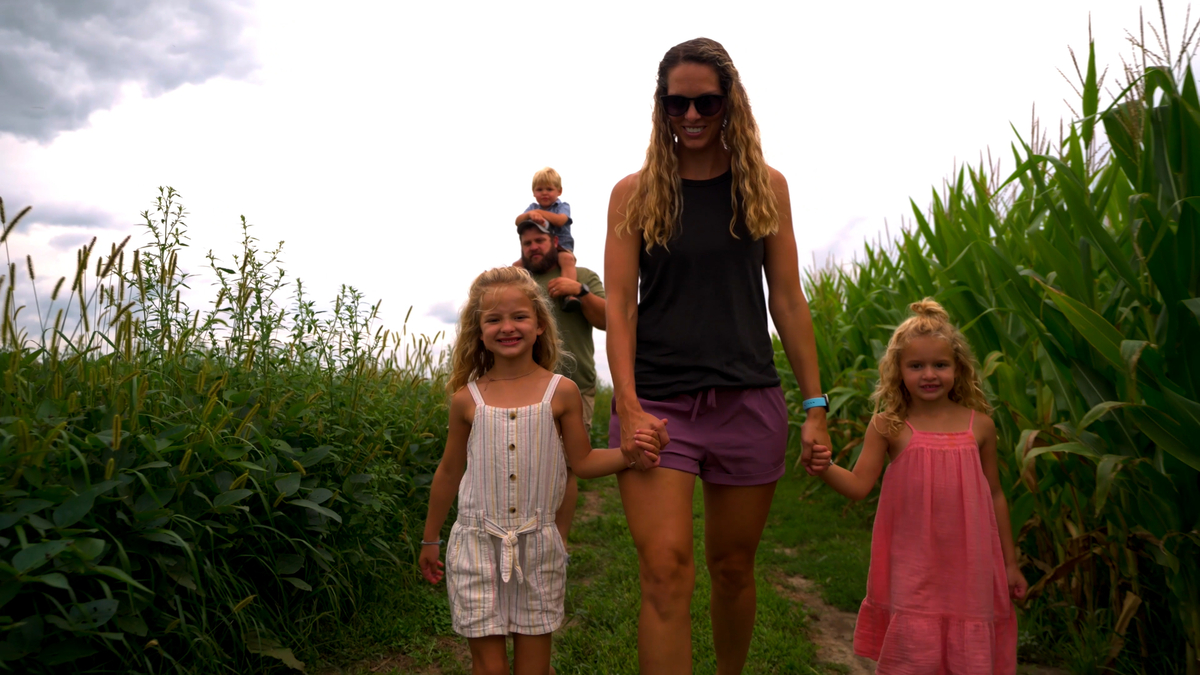 Family walks through a field and mom is holding hands with her kids