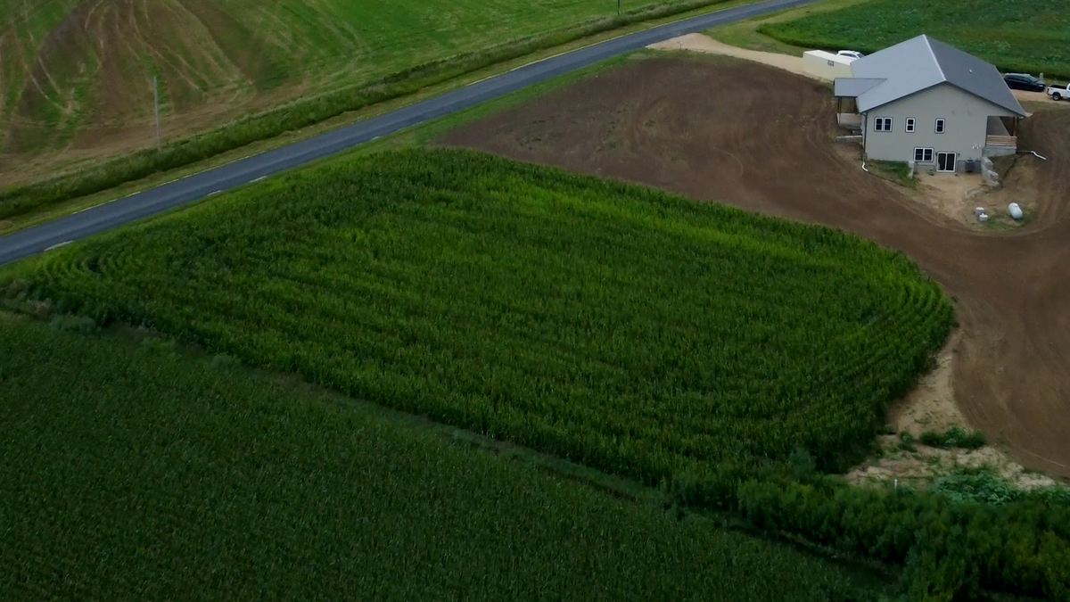 An aerial view of a tan barndominium-style home built next to farmland crops