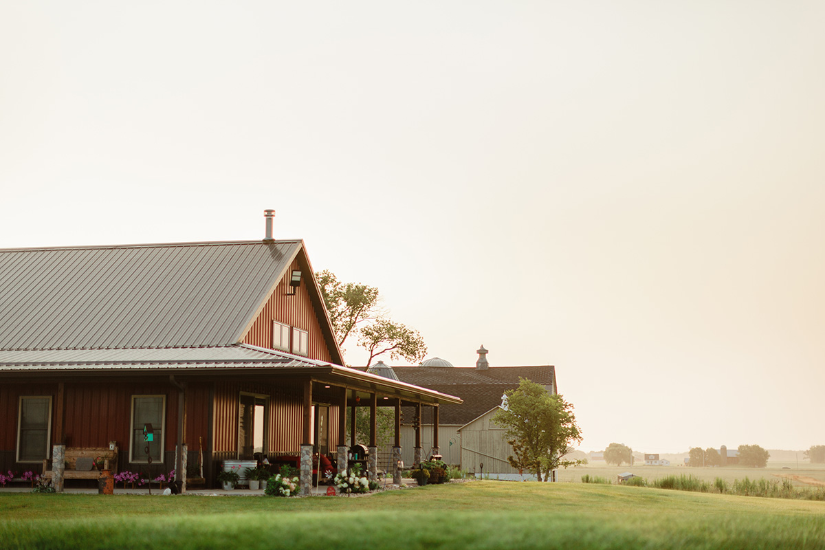 A warm-toned barndominium home with a wraparound porch and metal roof