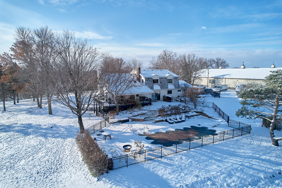 High-angle winter view of farmstead, outbuildings and surrounding fields covered in snow.