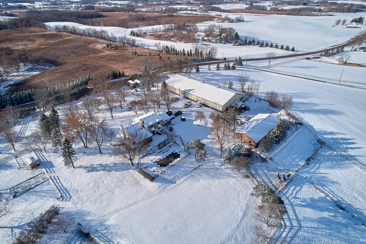 Aerial view of country home, fenced pool and barn in snow.