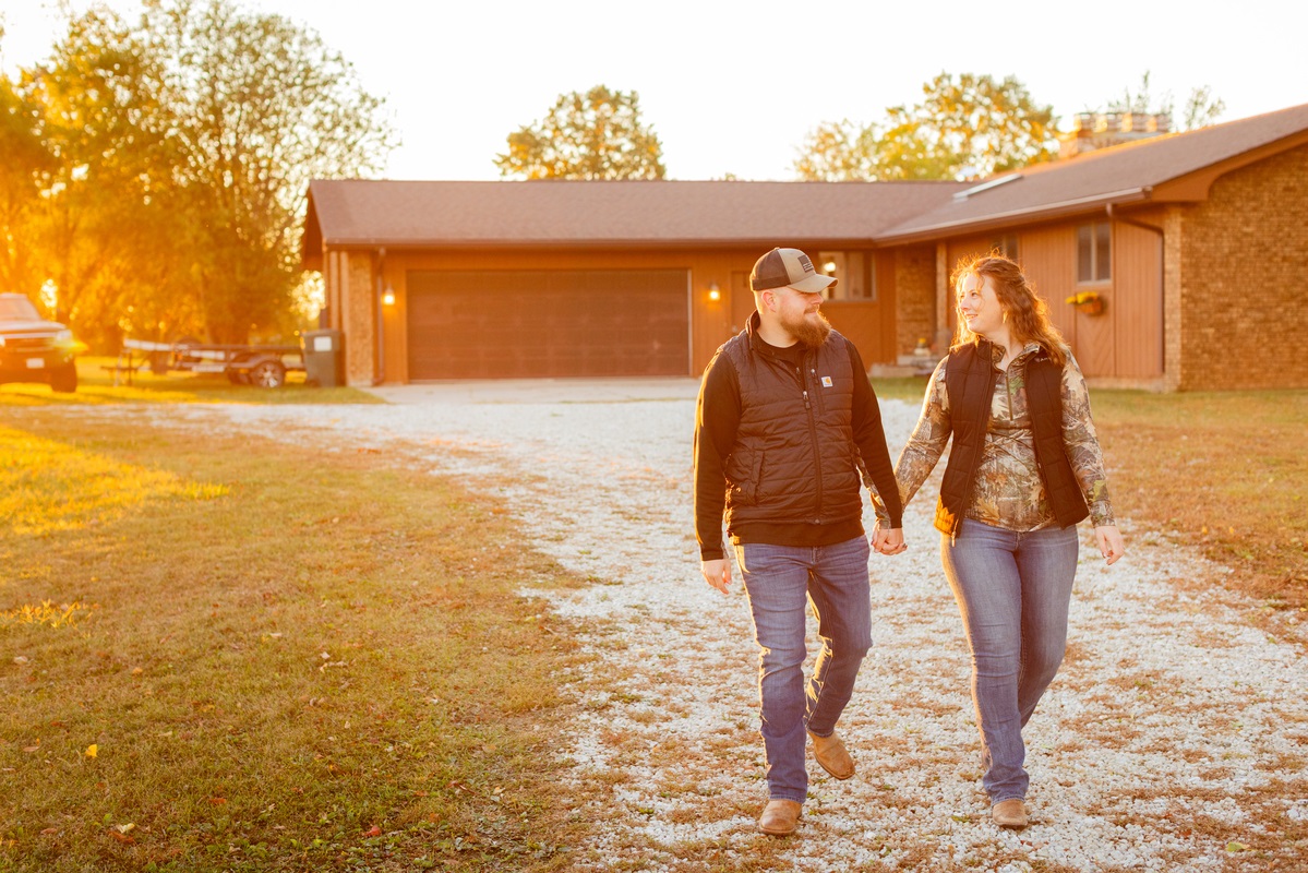 Couple walking hand in hand away from their home at sunrise on a gravel drive. 