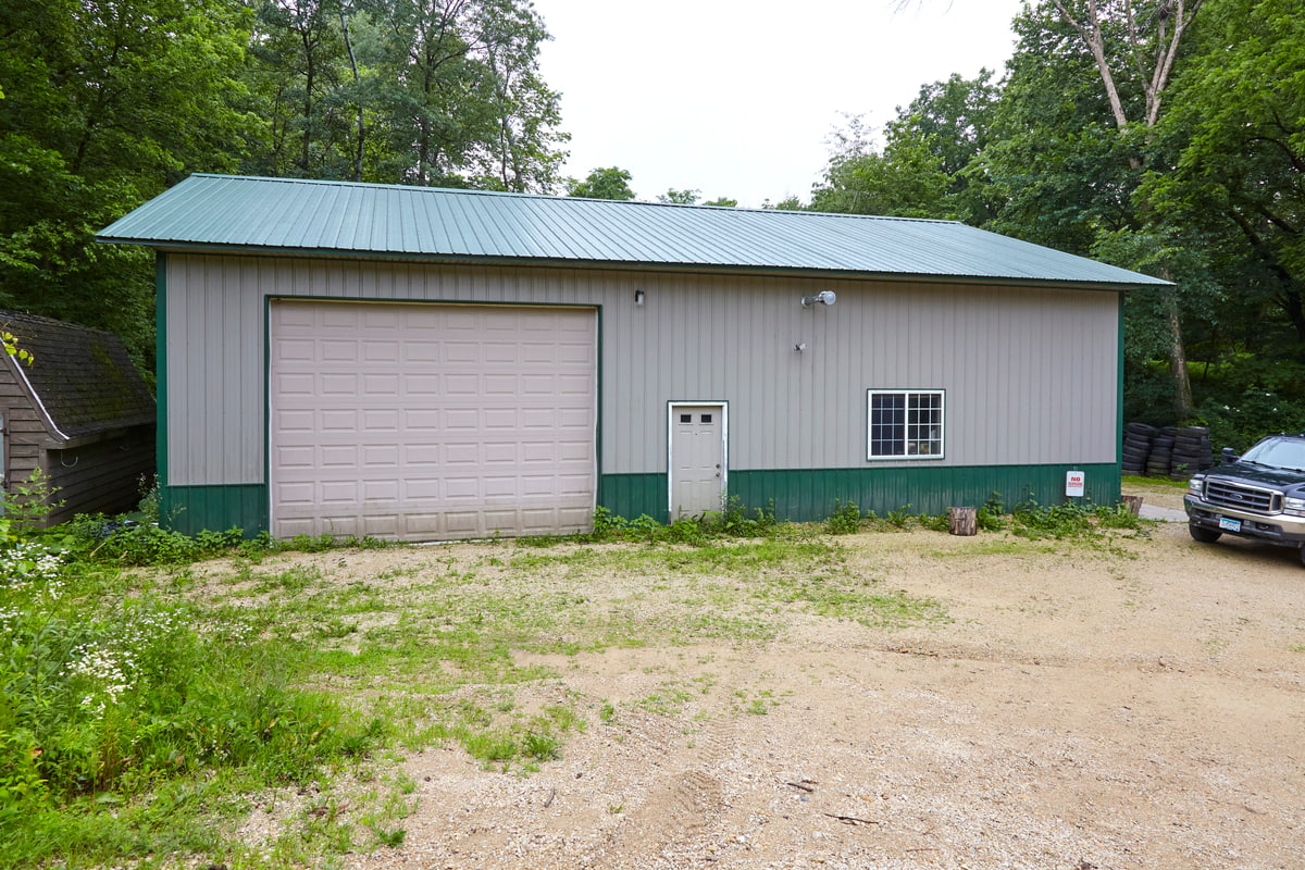 A large gray pole shed with a green roof and trim featuring a beige garage door and side entry door.
