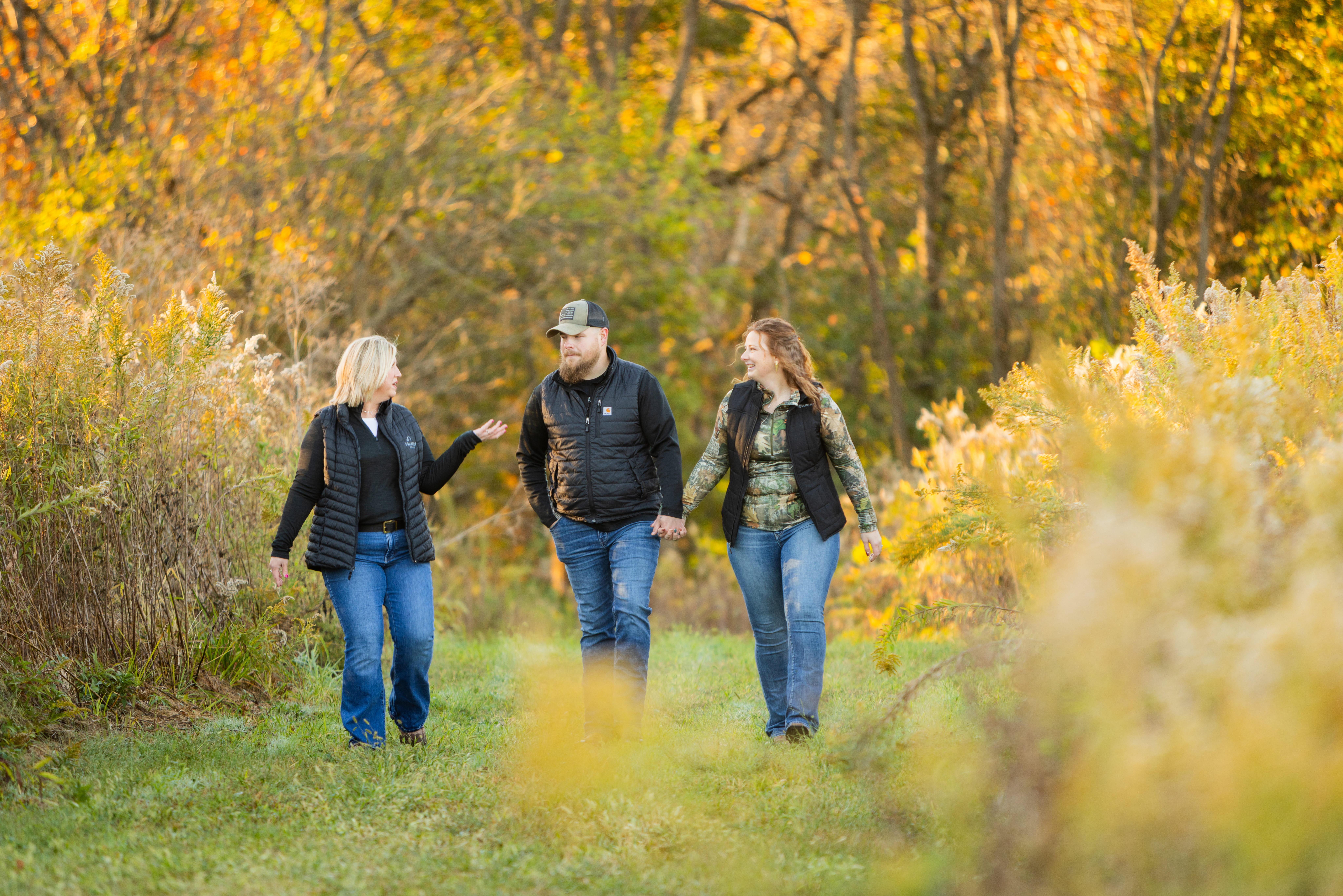 three people walk down a wooded path