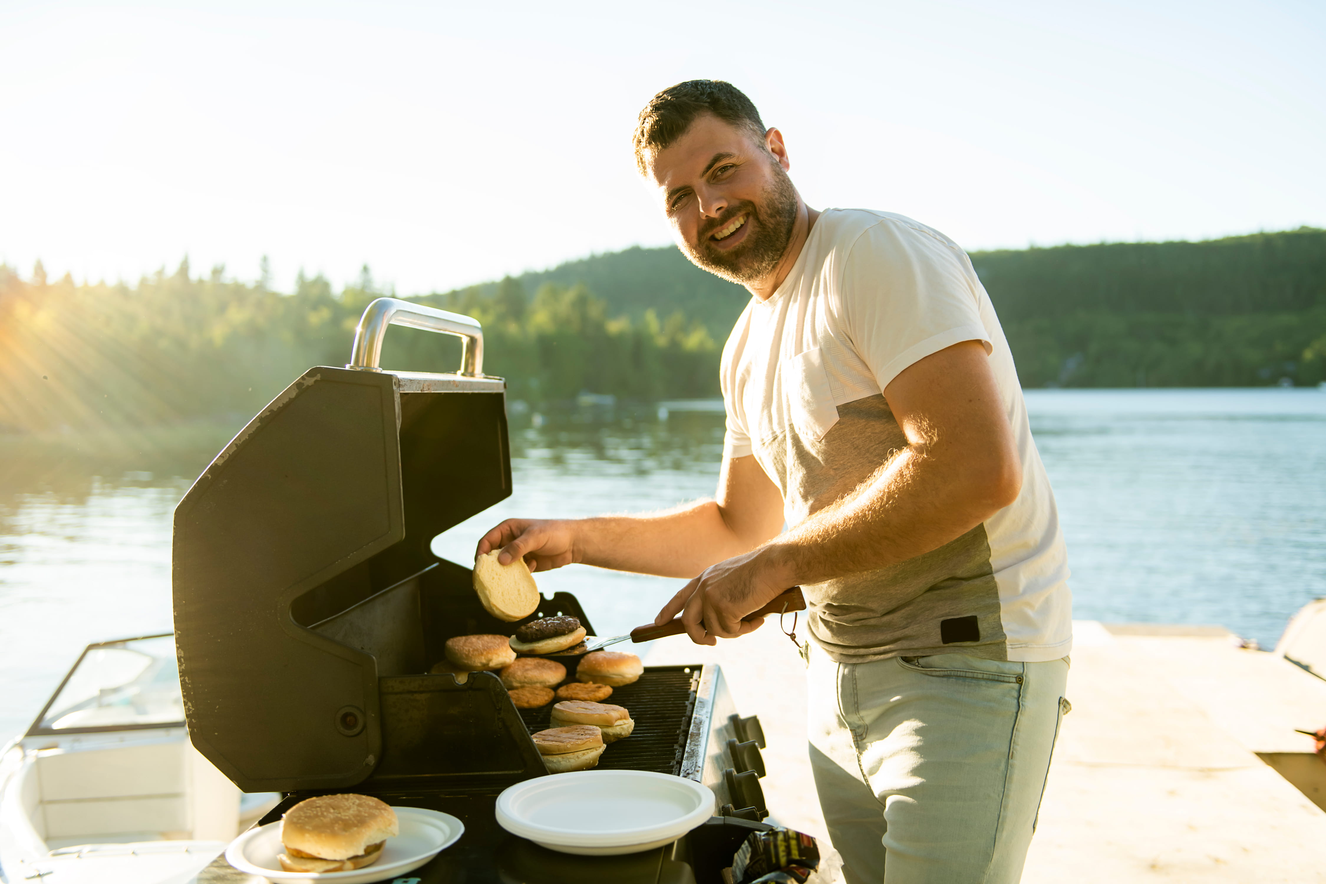 Man grilling burgers by a lake.