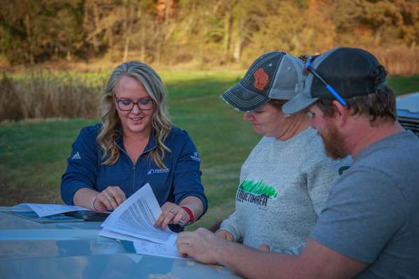 A man and woman leaning against a car hood reviewing mortgage documents