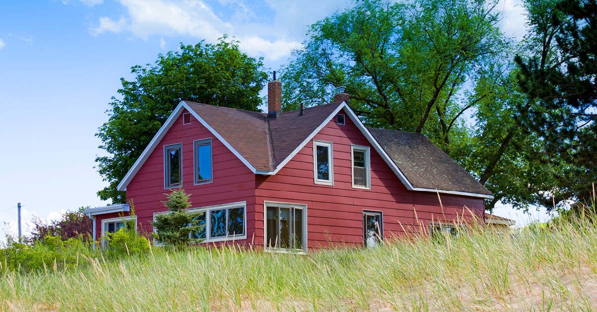 A red barn with brown fence surrounded by trees on a rural home property