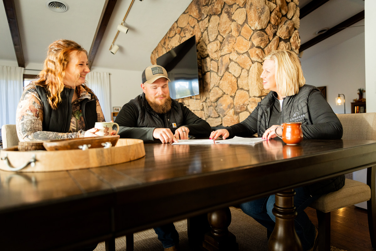 Couple meeting with a loan officer at home, reviewing paperwork and smiling.