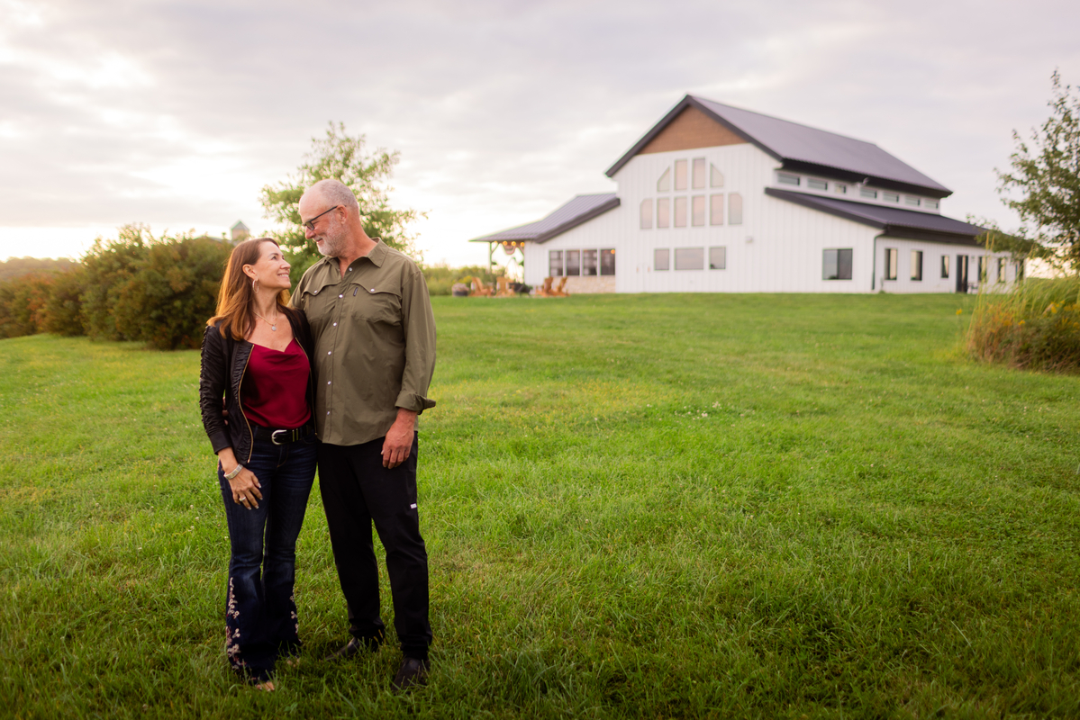 Couple standing together on a grassy lawn in front of a modern white barndominium.
