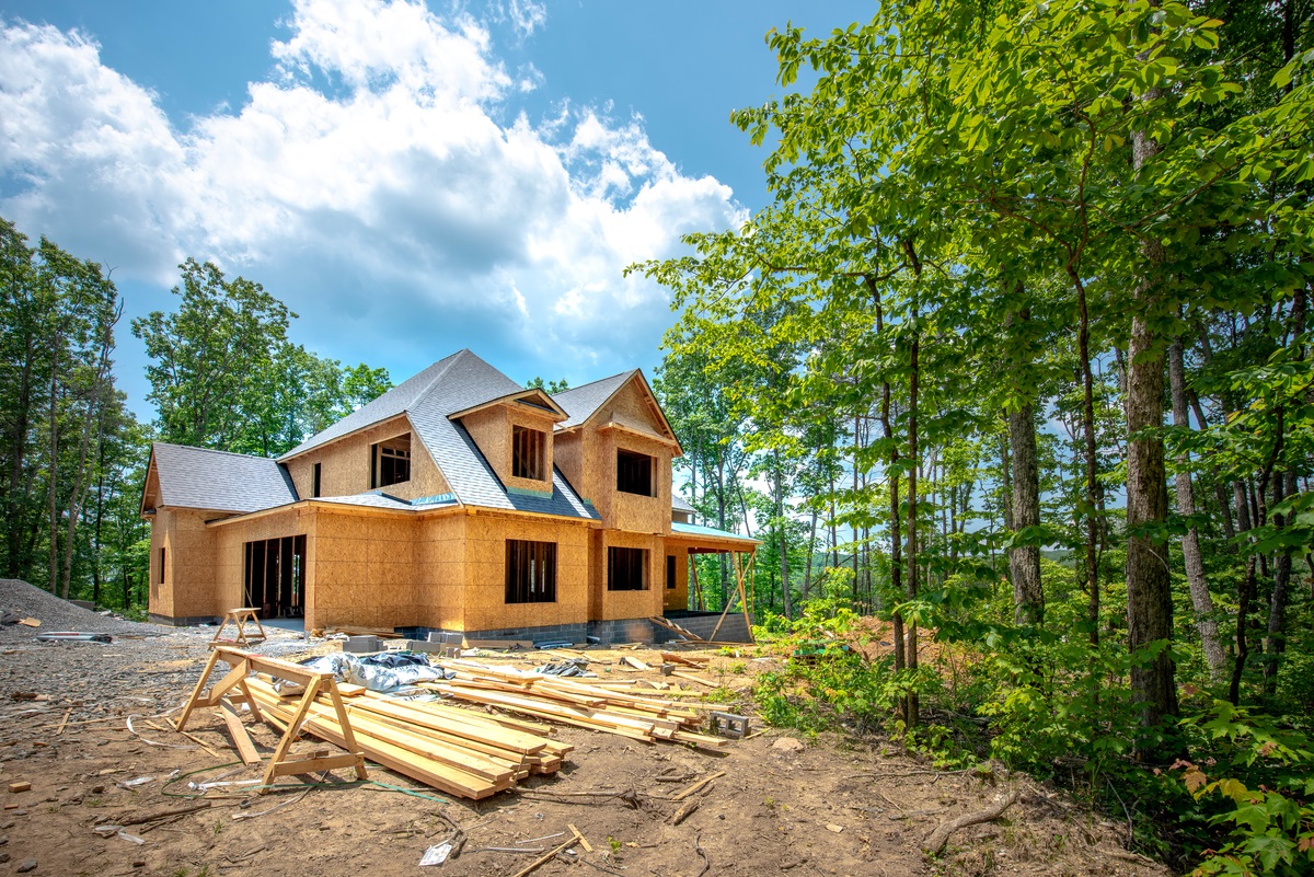 New home under construction surrounded by trees with lumber stacked in the yard.