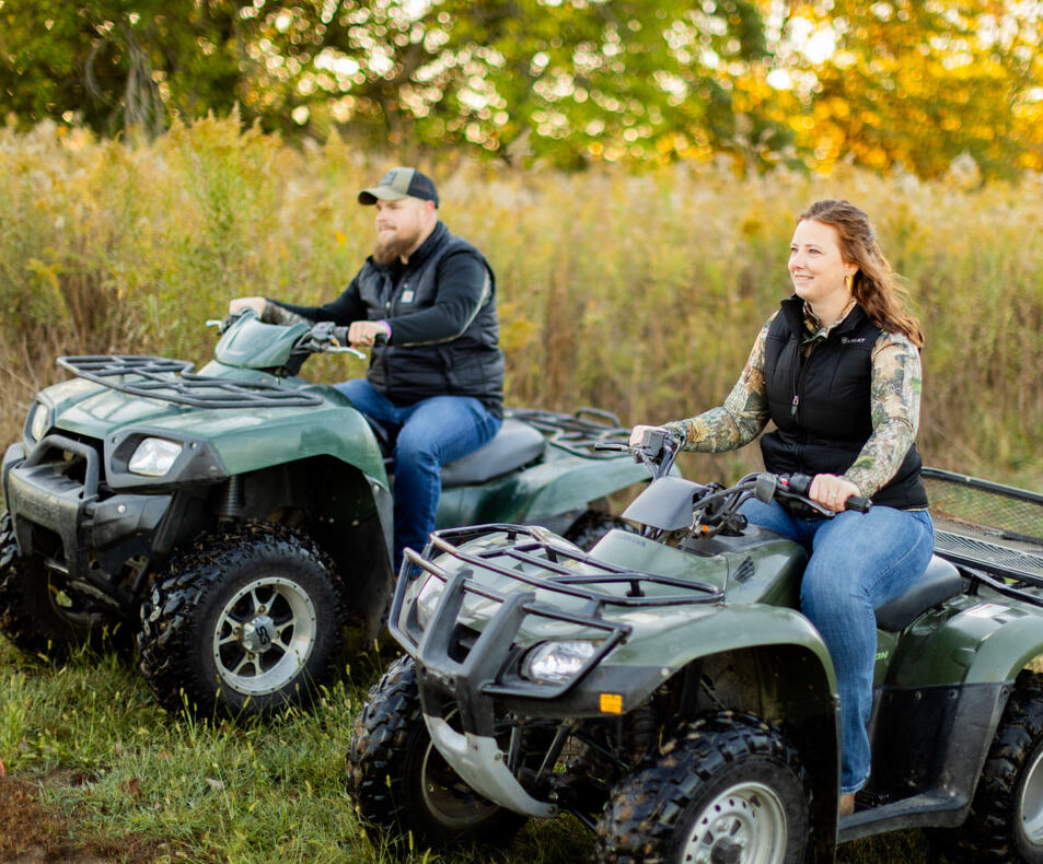 Couple riding all-terrain vehicles across grassy recreational land property during golden hour.