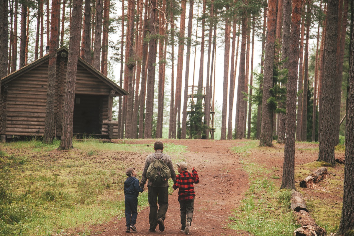 Man and two children walking on a path towards a rustic cabin,