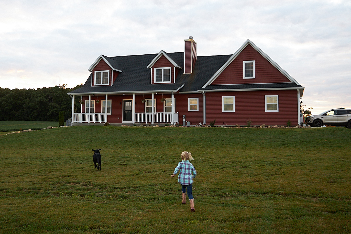 farmhouse with wraparound porch and horses in the yard