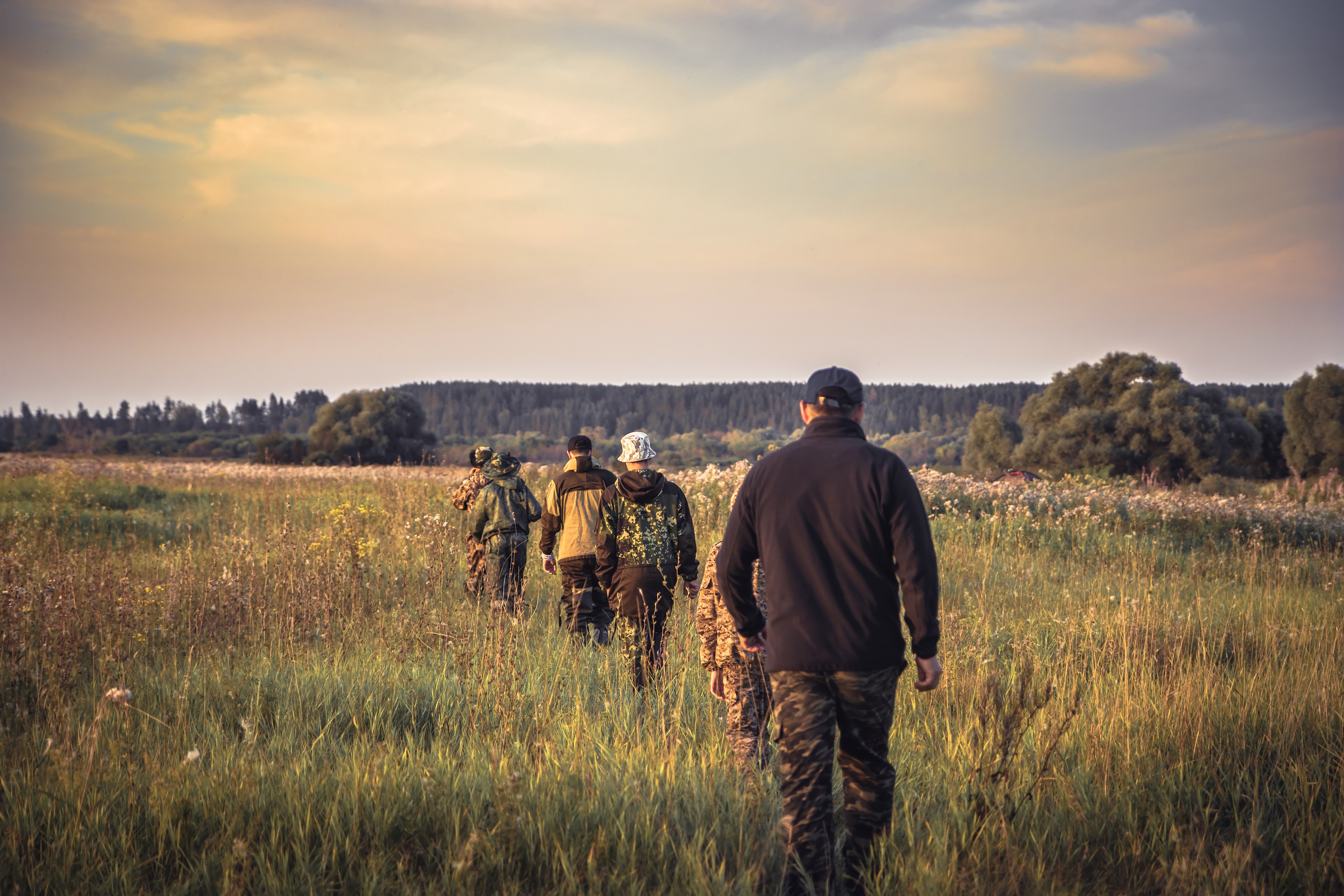 A group of hunters dressed in camo walk through a grassy field