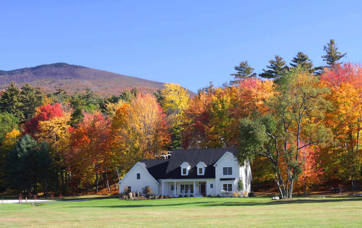 White rural home surrounded by colorful autumn trees under a bright blue sky.
