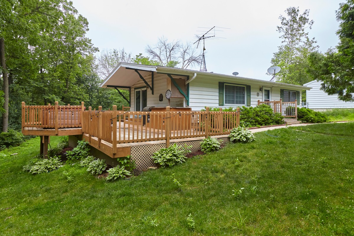 A spacious wooden deck extends from a white mobile home surrounded by greenery and trees