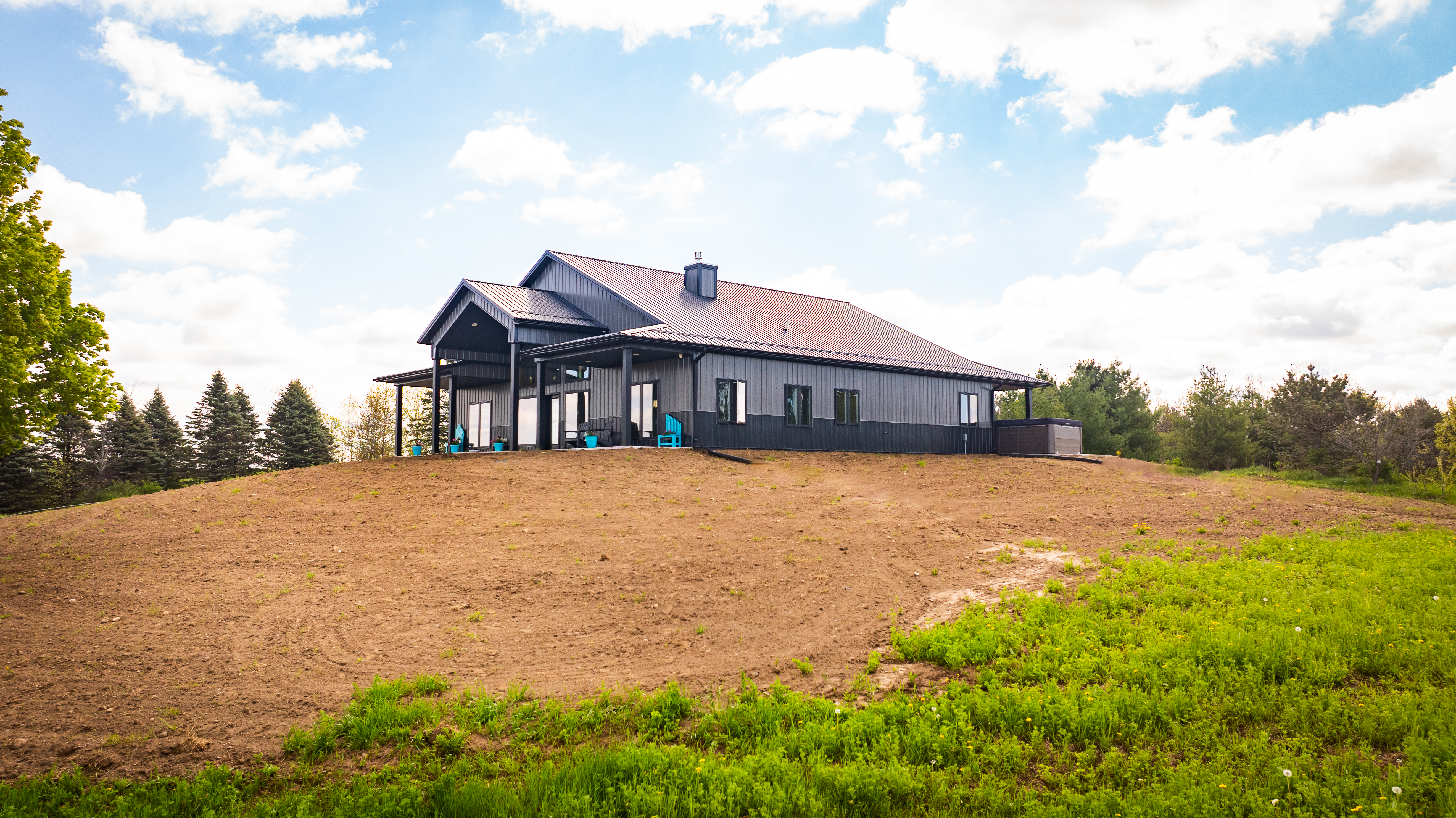 Modern barndominium with metal roof on a hilltop beneath a bright sky.