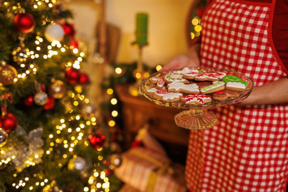 Person holding a plate of decorated Christmas cookies beside a lit holiday tree.