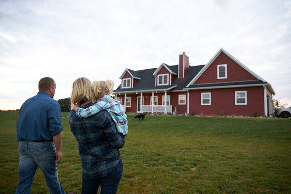 Parents and child walk across lawn toward a red farmhouse at dusk.