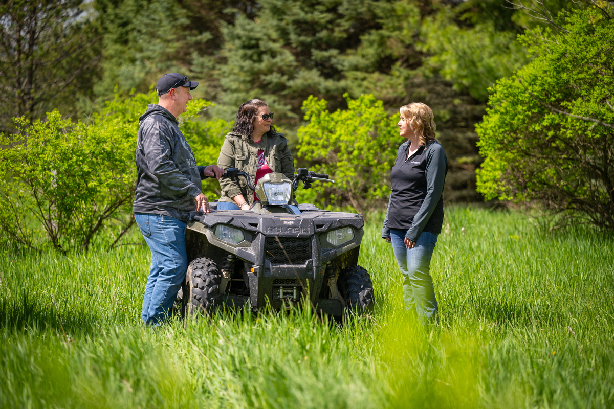 Three adults talking around an ATV in a field