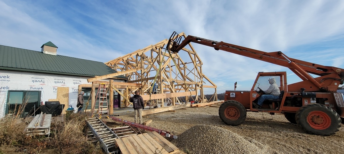: Construction crew raising a barndominium frame using heavy equipment on a clear day.
