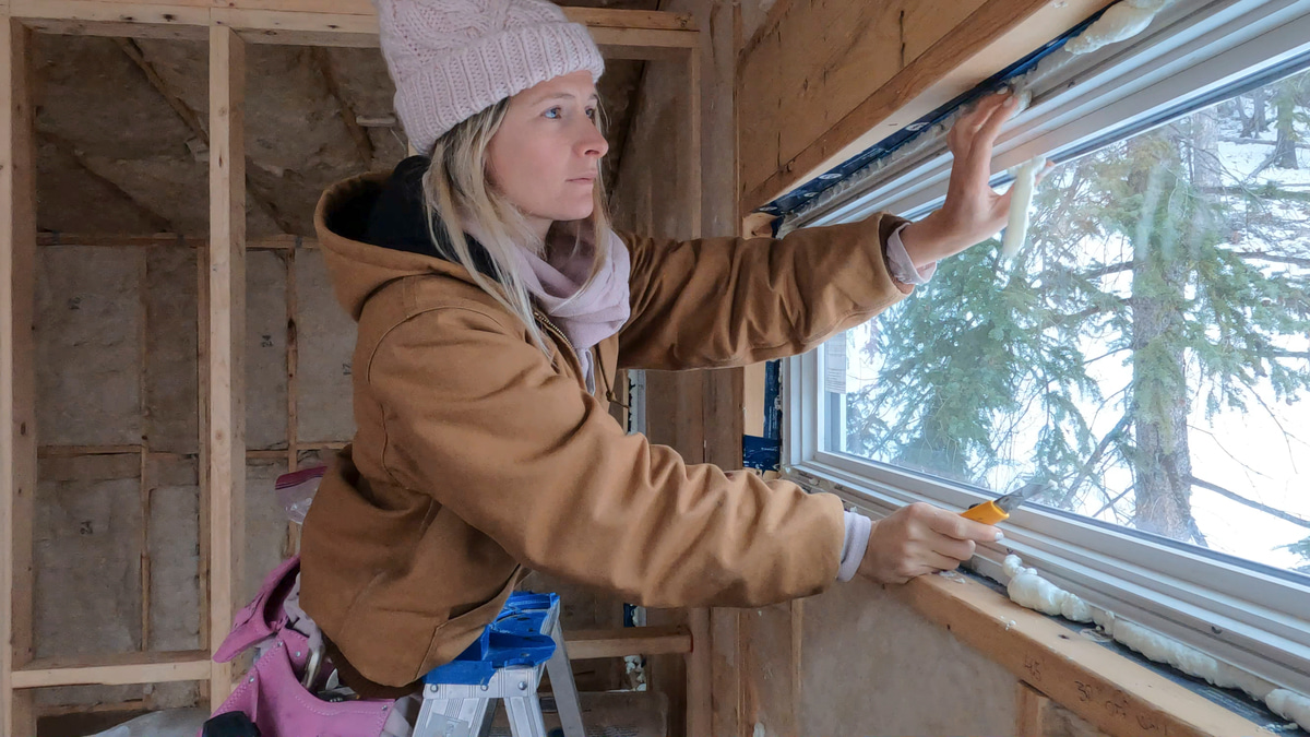 Woman applying insulation sealant around a window to reduce winter drafts indoors.