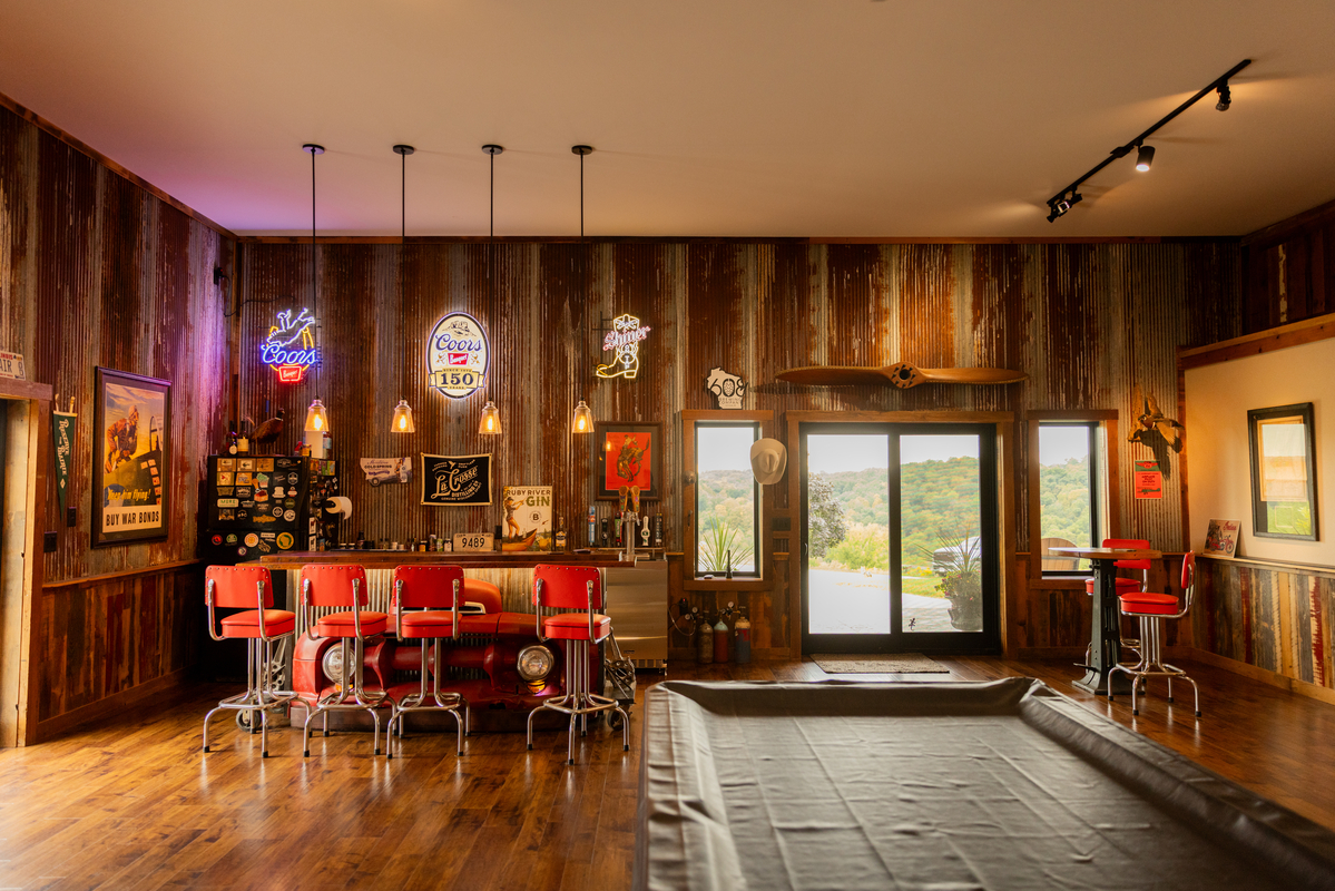 Rustic home bar with neon signs, vintage decor, and red stools overlooking scenic views.