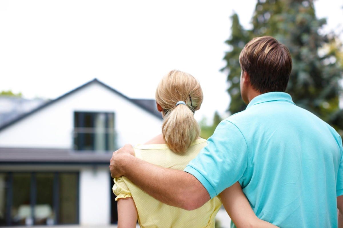 Man and woman with arms around each other looking at a house