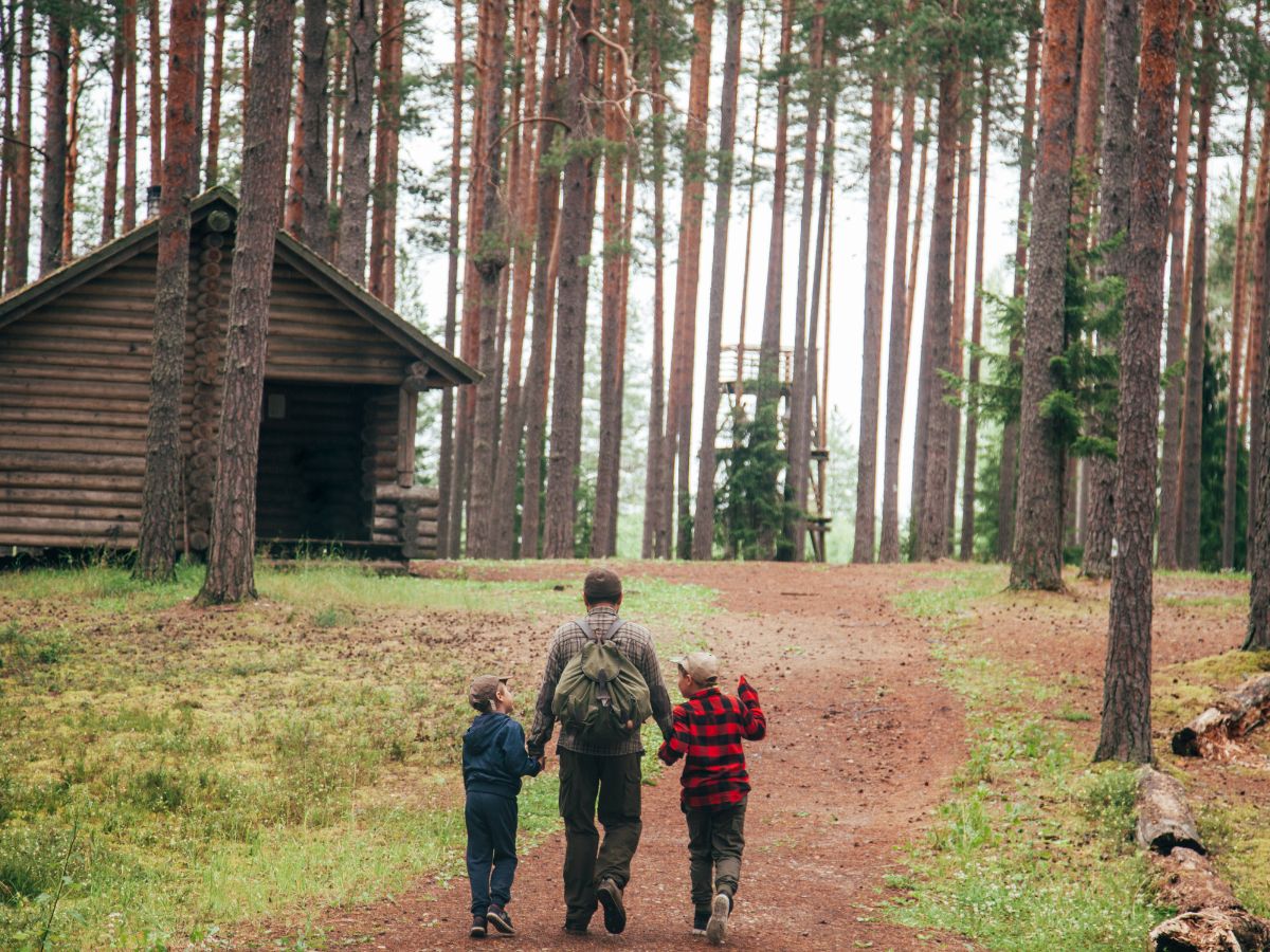 Dad and two kids walking up a path to a log cabin
