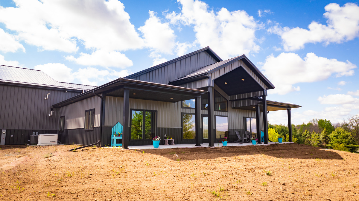 Modern barndominium with metal roof on a hilltop beneath a bright sky.