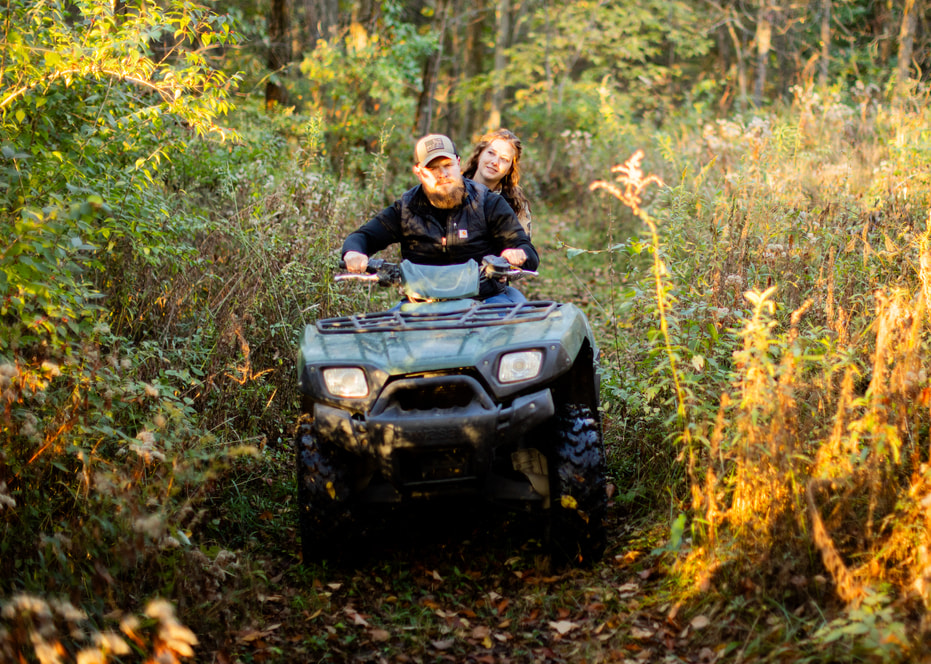 Man and woman driving through wooded rural land on a UTV