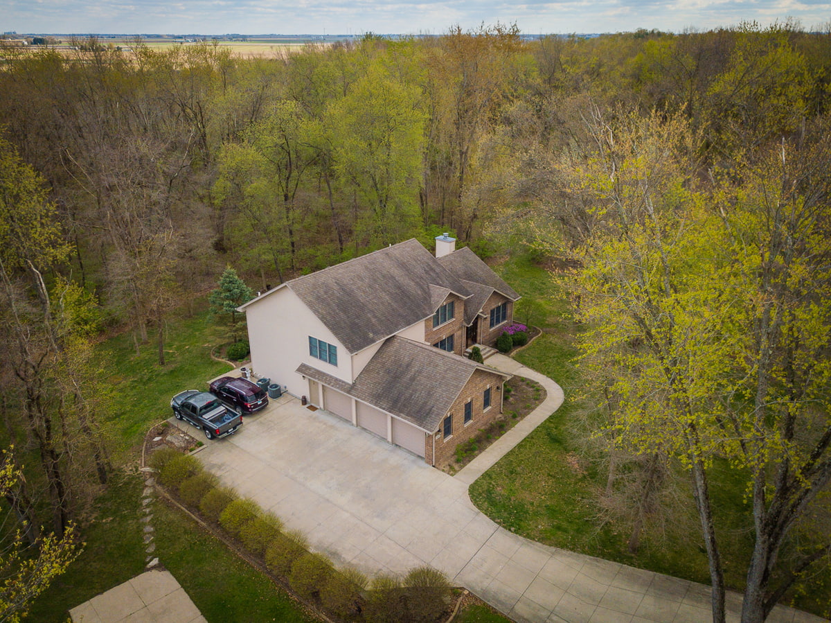Aerial view of a large home with driveway surrounded by dense wooded acreage.