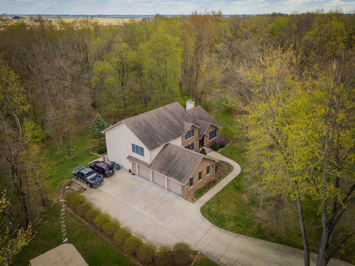 Aerial view of a large home with driveway surrounded by dense wooded acreage.
