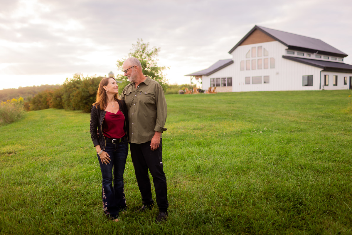 Couple standing together on a grassy lawn in front of a modern white barndominium.