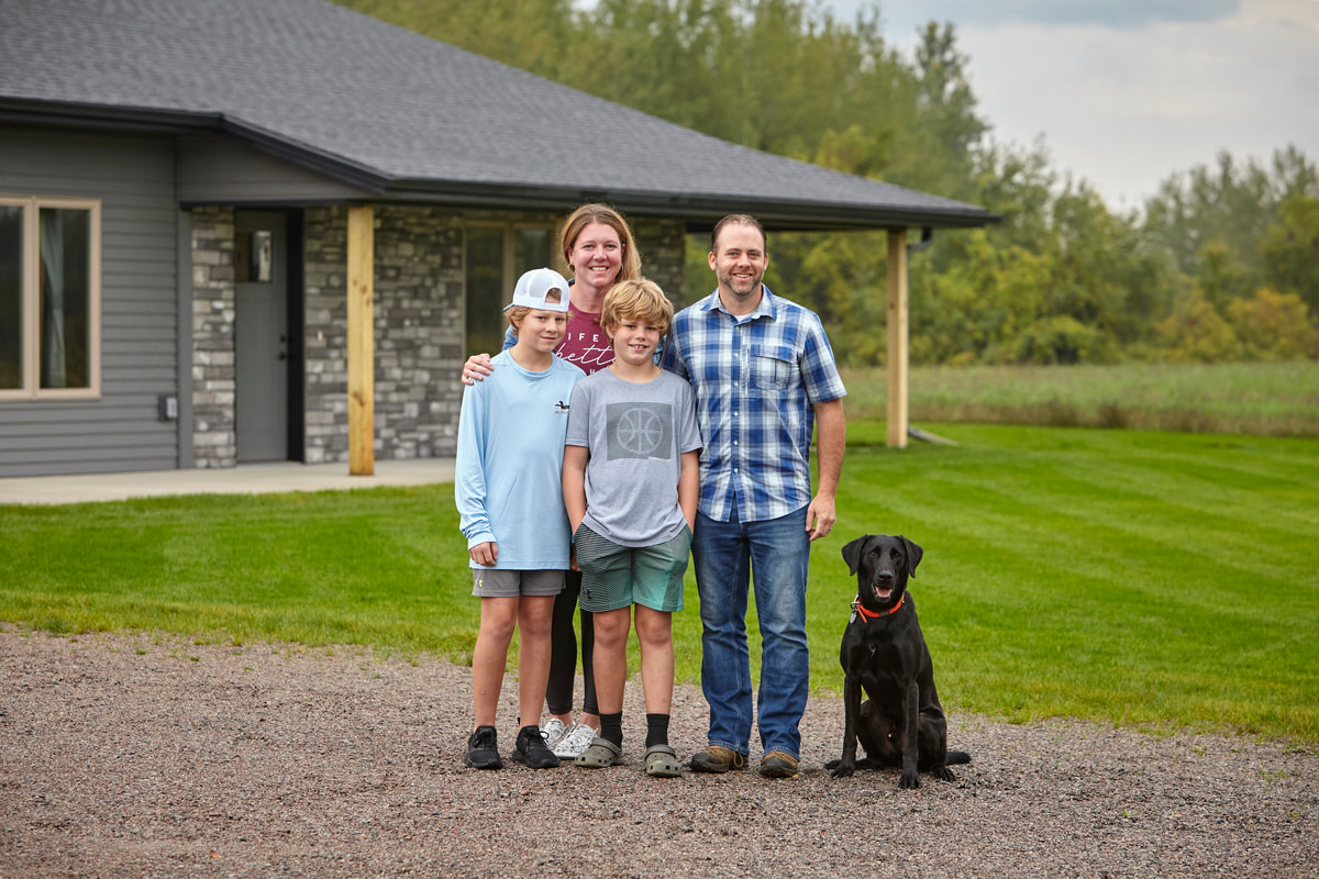 Family standing with their black dog in the driveway in front of their house