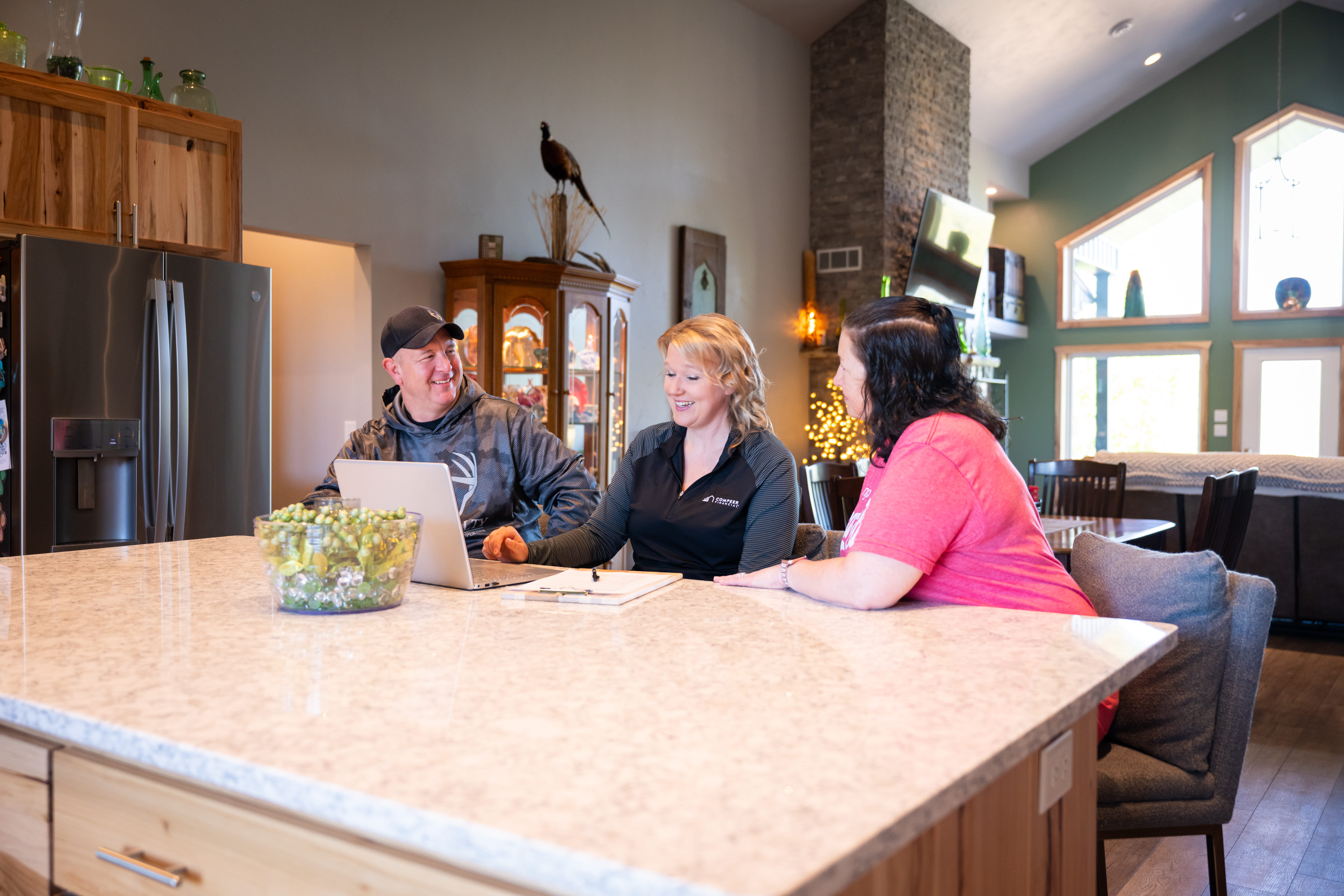Three people sit at a counter and talk next to a computer